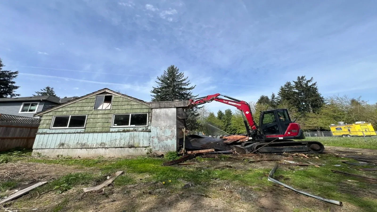 Compact excavator tearing down a small shingled house