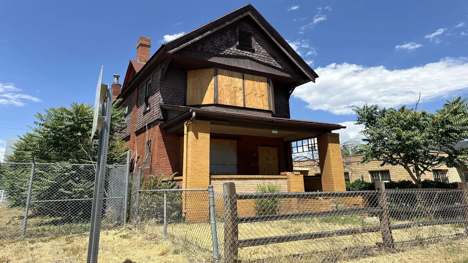 Older boarded-up two-story house standing behind a chain-link fence