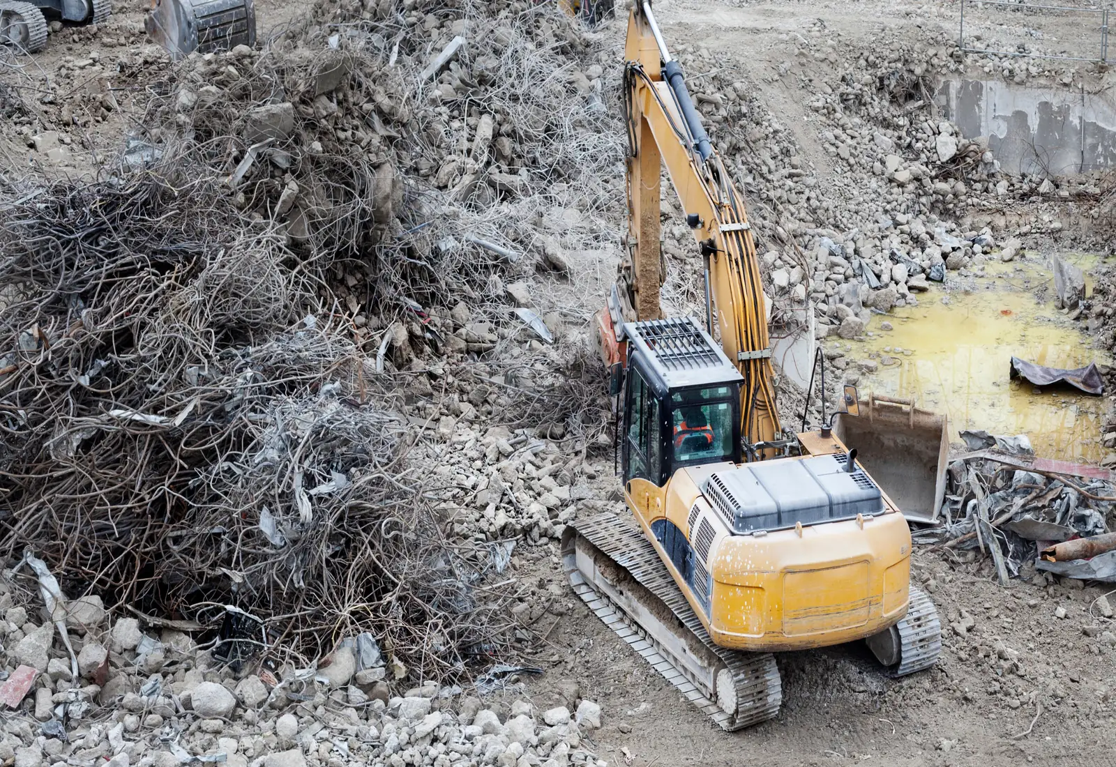 Excavator on a commercial demolition site with separated piles of concrete and scrap steel