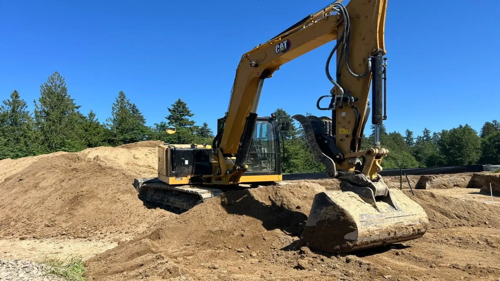 Excavator parked on a spoil pile on an open work site under a clear sky