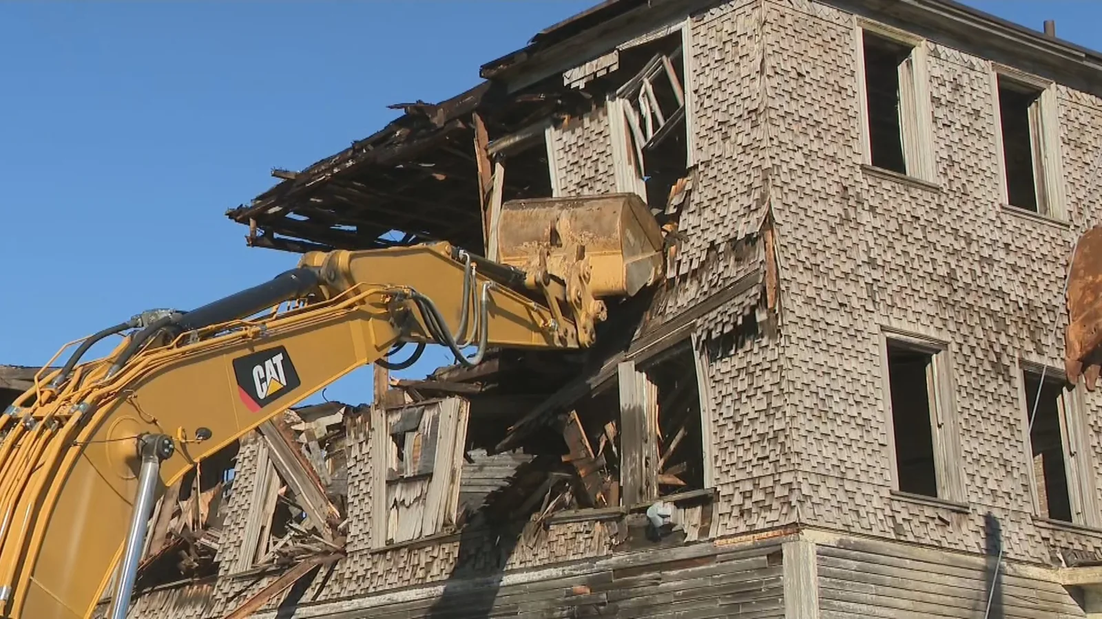 Excavator bucket tearing the upper story off a shingled building