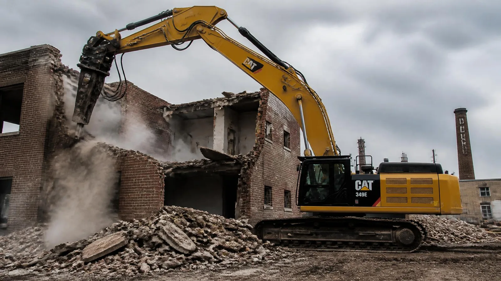 Excavator with a hydraulic hammer breaking down a brick industrial building