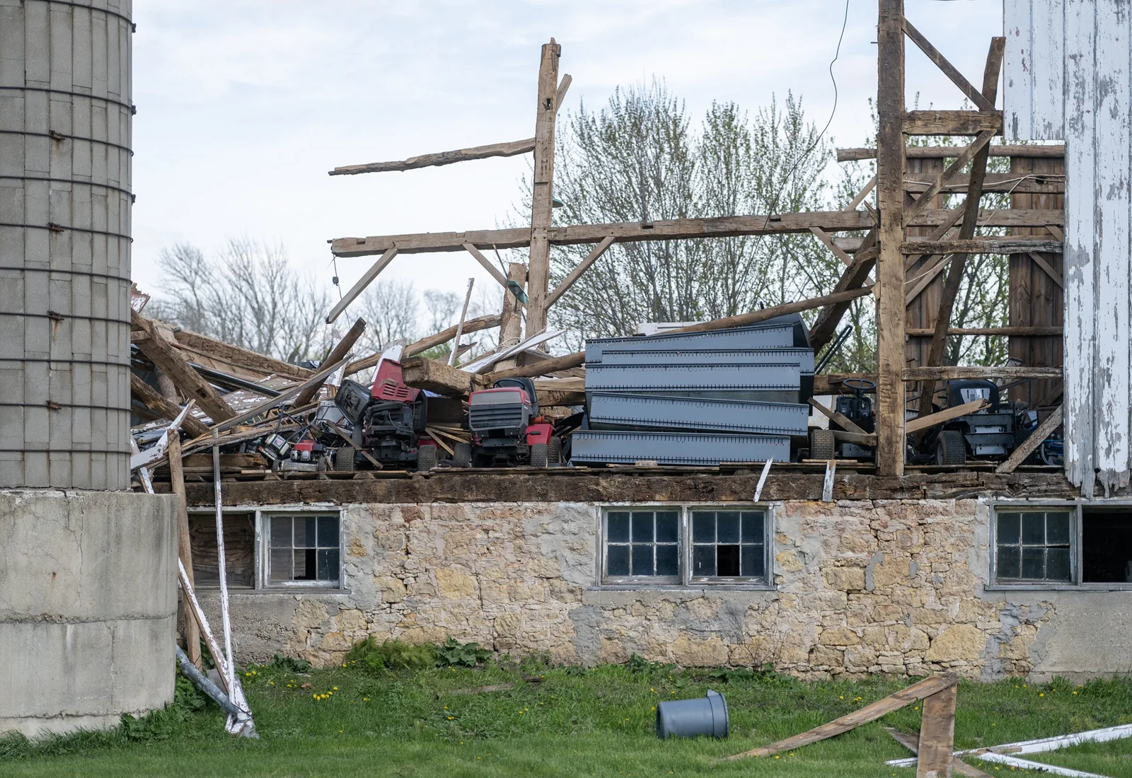 Old timber-frame barn collapsing onto its fieldstone foundation next to a silo