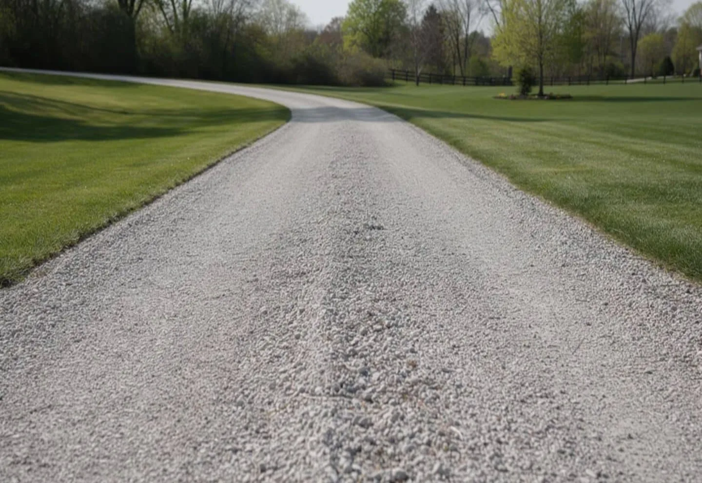 Finished crowned gravel driveway running between mown lawns toward a tree line