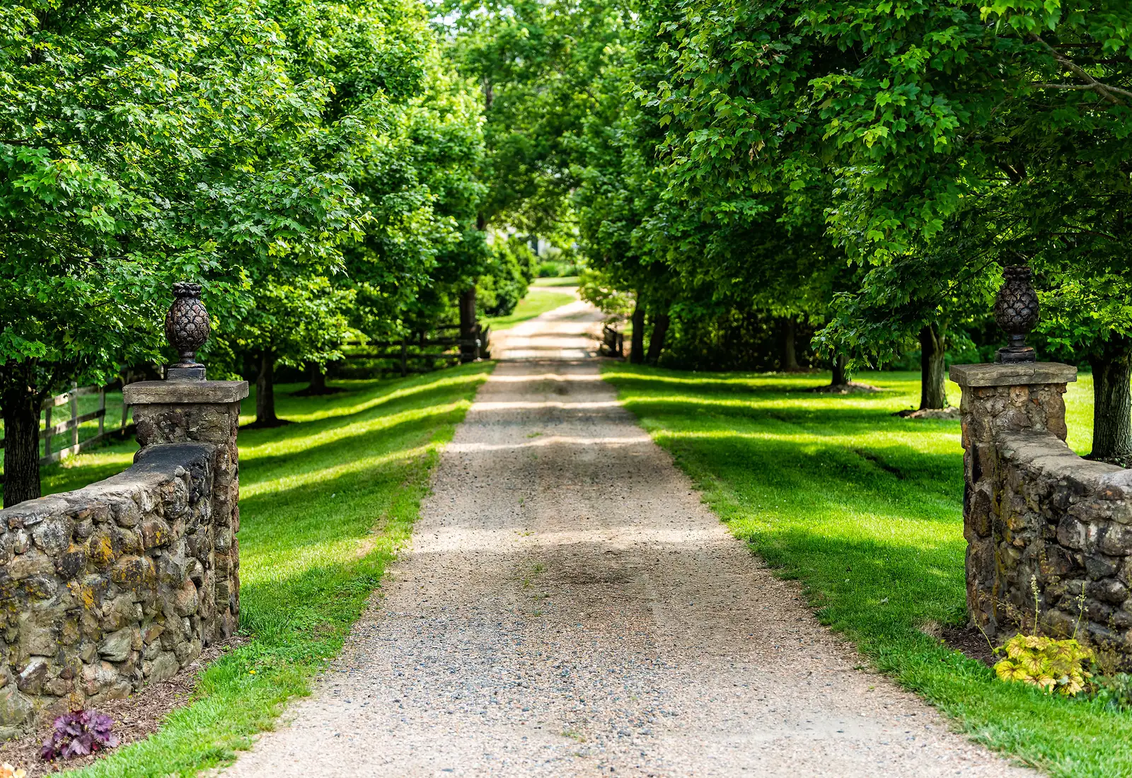 Long gravel driveway running between fieldstone pillars and a tree-lined lawn