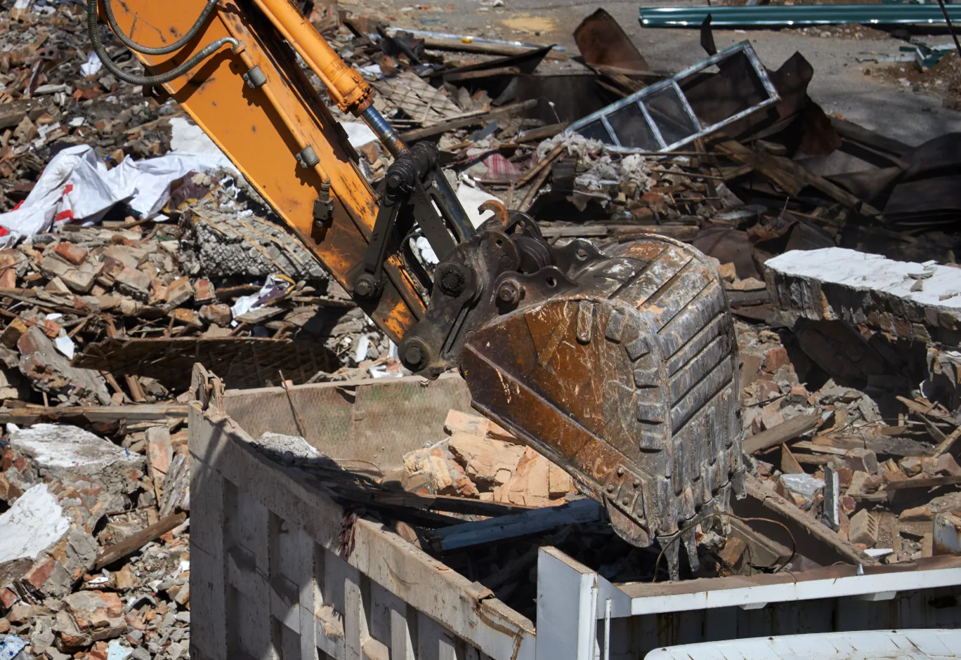 Excavator bucket lifting broken wood and masonry debris into a dump body