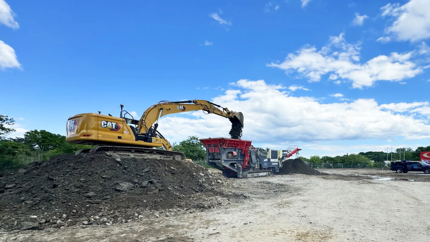 Excavator feeding a crusher from a stockpile of broken concrete on an open yard