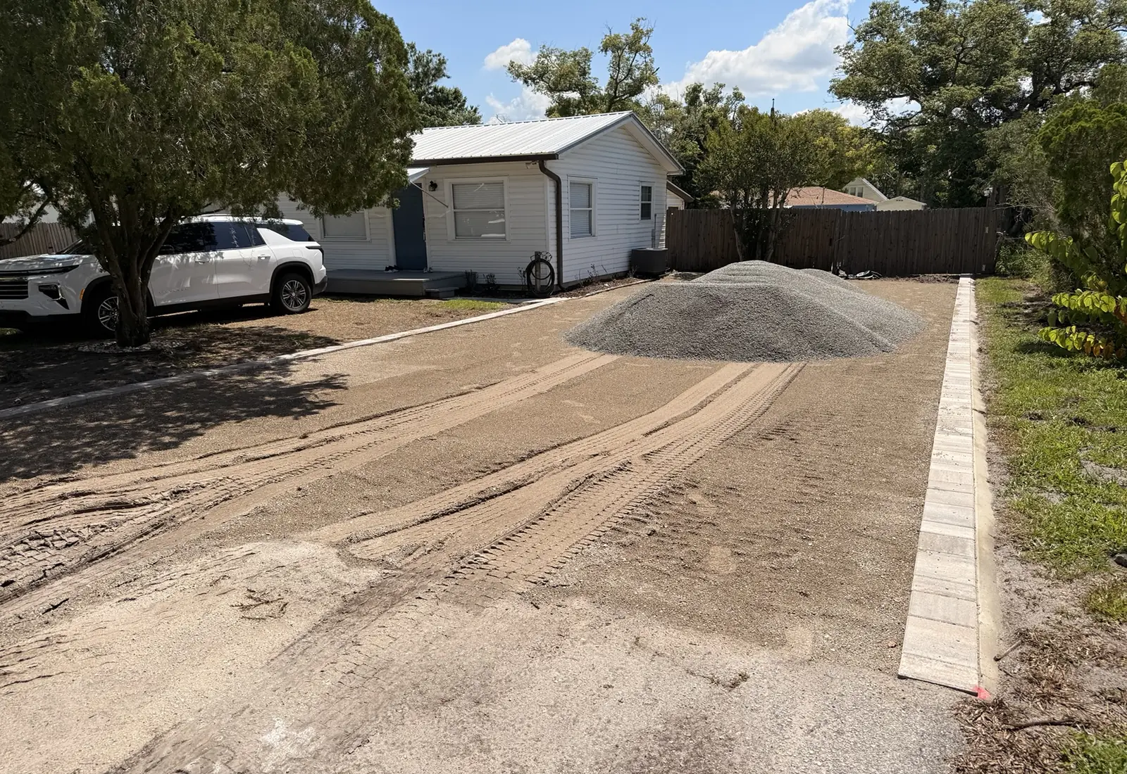 Rough-graded house site with a gravel driveway cut in and a stockpile of stone